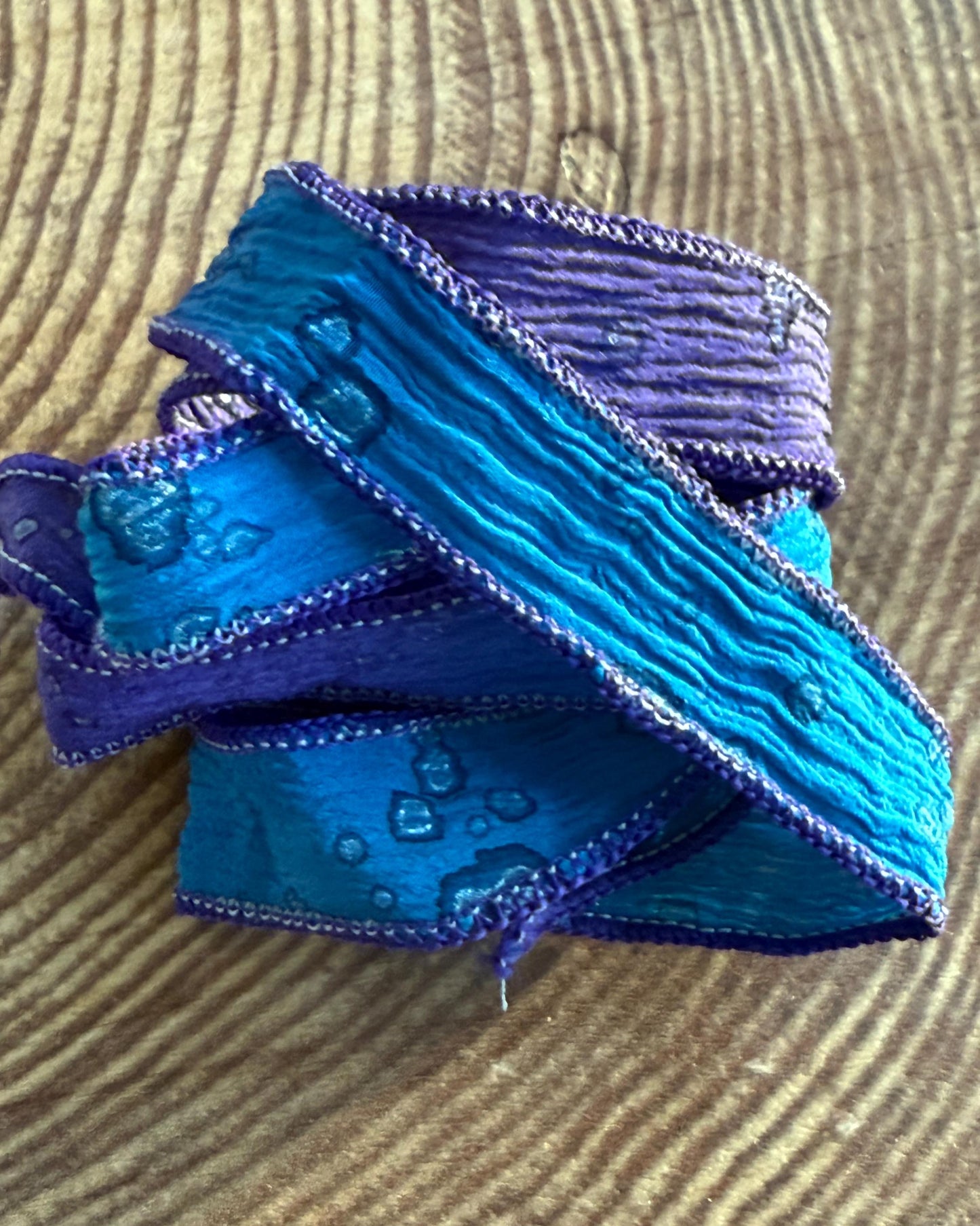 A silk wrap ribbon with blue and purple hues, sewn to a point, displayed on a textured background.