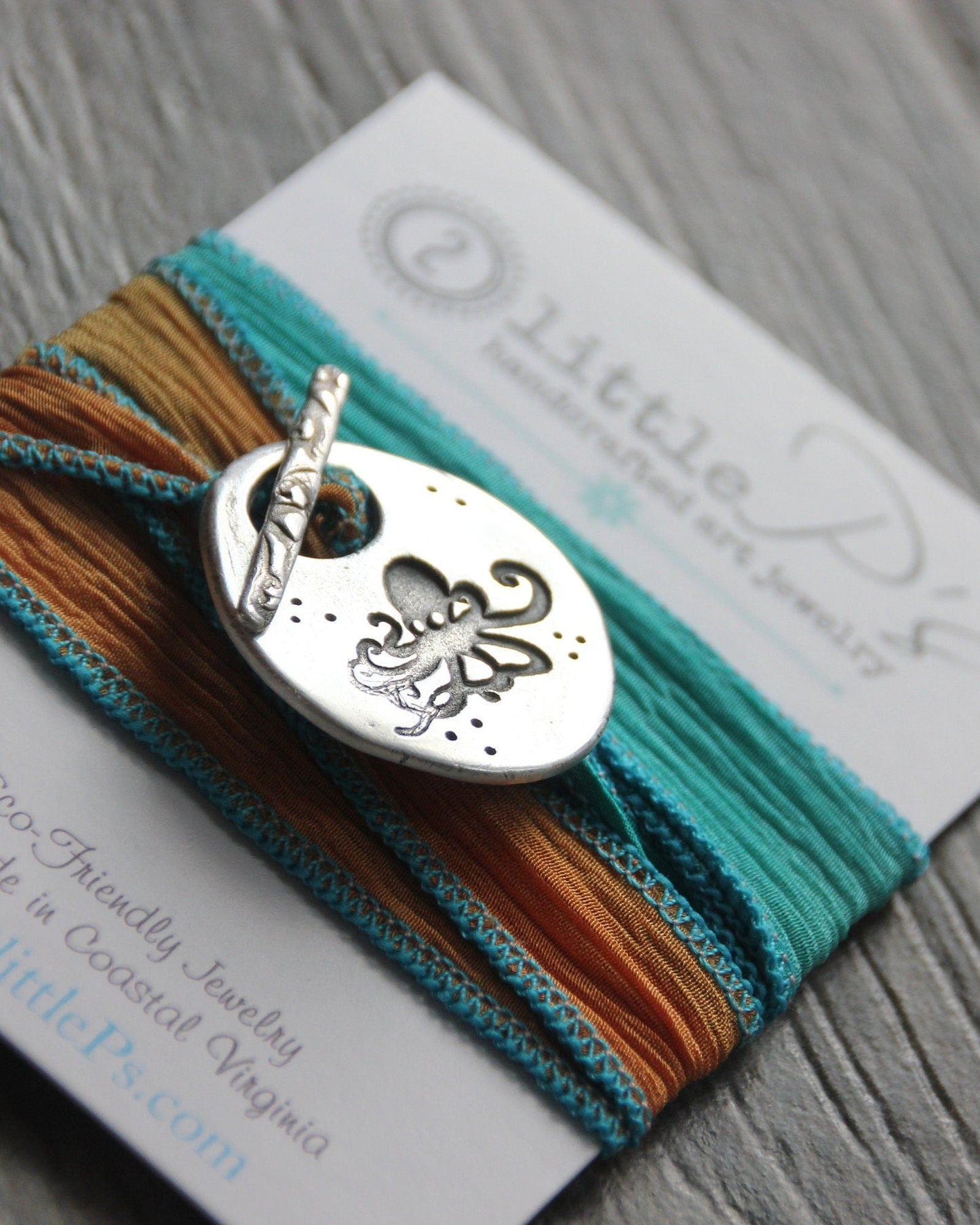 A handcrafted pure silver octopus toggle bracelet with hand dyed shades of coral and teal sari ribbon, displayed on a card with the brand name 2 Little P's.