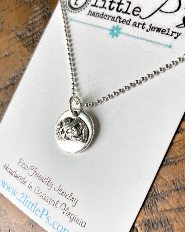 A Comedy and Tragedy charm pendant made of pure silver, displayed on an 18 inch oxidized sterling silver bead ball chain, packaged on a card with the 2littleps brand details.
