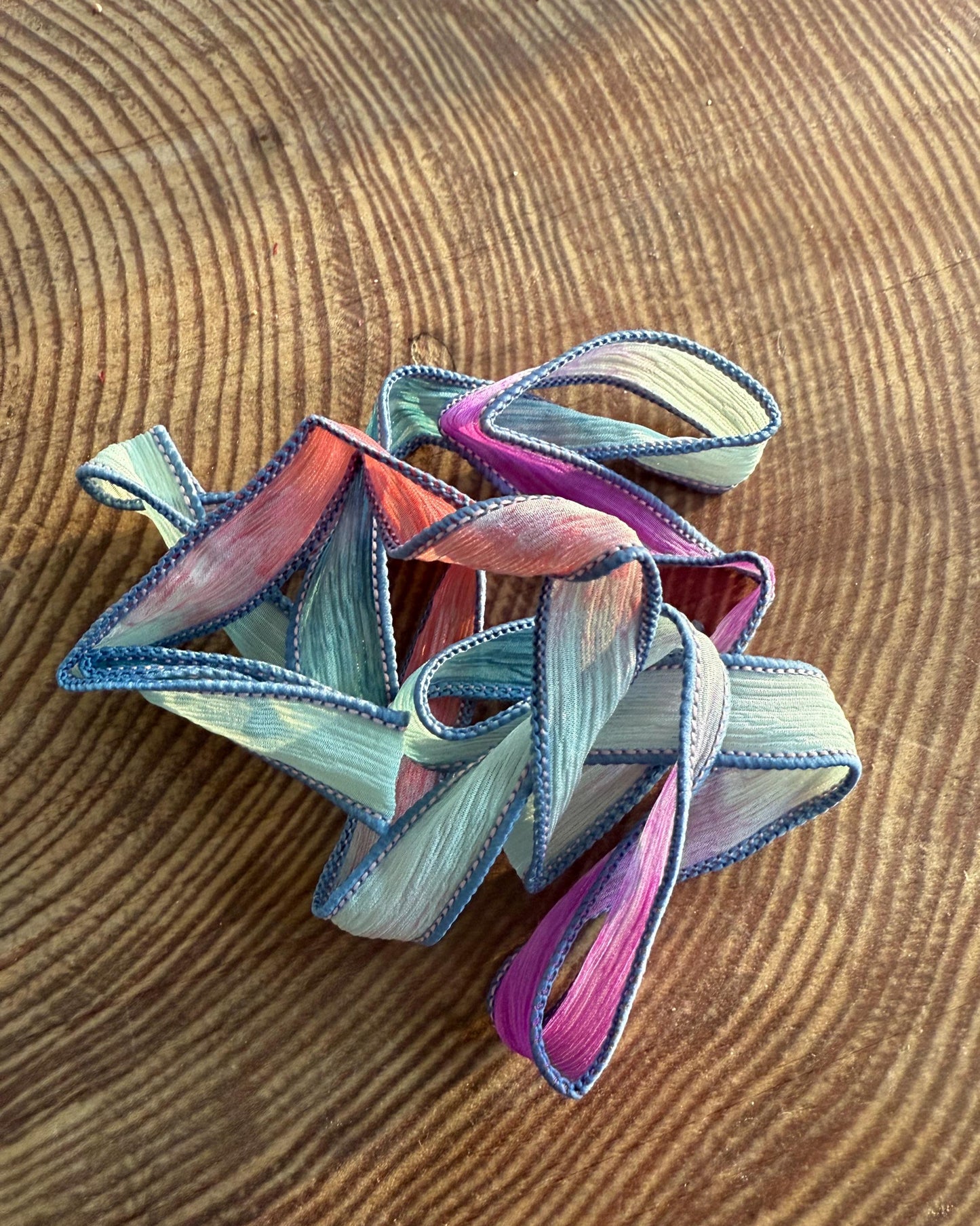 A crinkled silk wrap ribbon in hues of lavender and jet black, sewn to a point, displayed on a wooden surface.