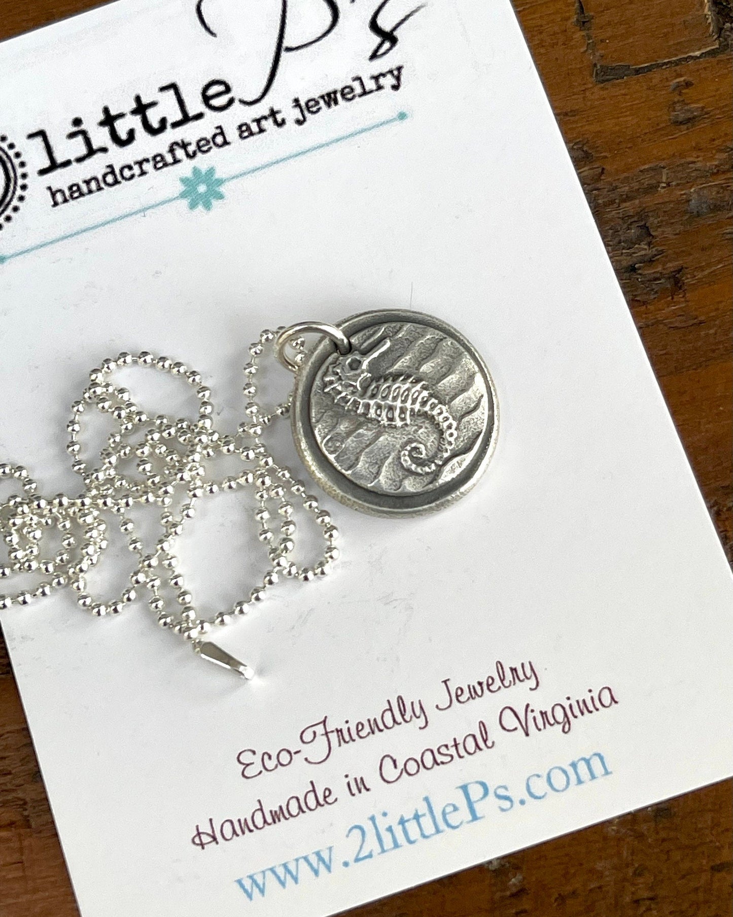 A handcrafted silver sea horse pendant necklace displayed on a card with the brand name 2 Little P's.