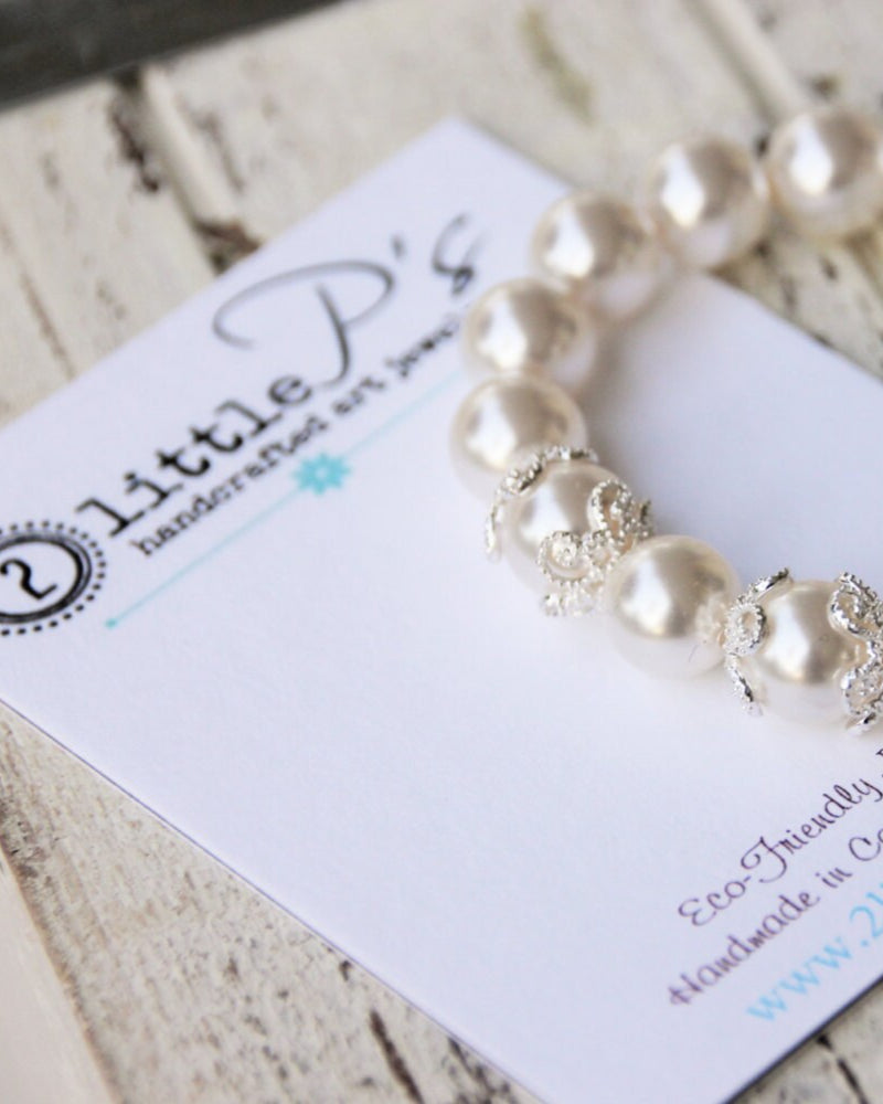 A handcrafted Swarovski Pearl Elements bead bracelet with sterling silver floral end caps, displayed on a white card with 2 Little P's branding.