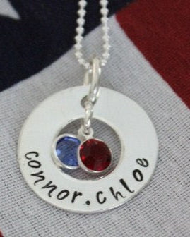 Handstamped sterling silver washer charm necklace with two Swarovski birthstone crystals, personalized with names, displayed against an American flag backdrop.