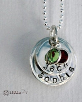A sterling silver handstamped necklace with two circular charms, one with 'BIG KID' and the other with 'LITTLE KID', surrounded by a Swarovski birthstone crystal on each charm, attached to a ball chain.