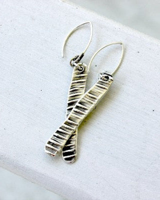 A pair of handcrafted pure silver textured earrings hanging on a white surface, with a small heart-shaped detail at the top.