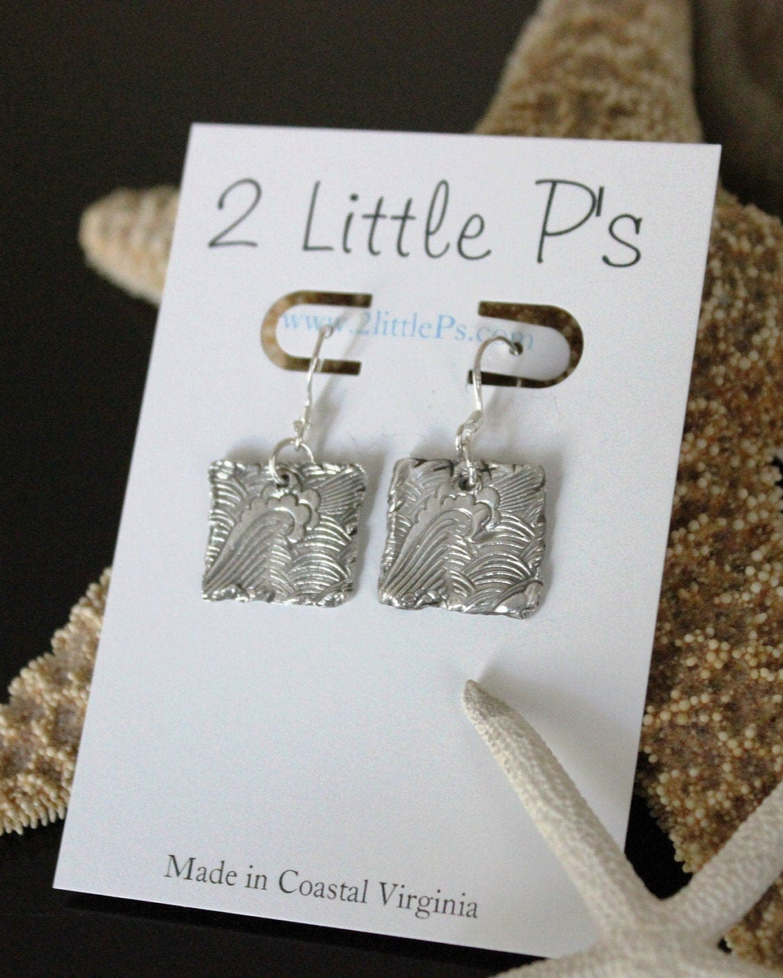 A pair of silver earrings designed to resemble ocean waves, displayed on a white card with '2 Little P's' branding and a note that they are made in Coastal Virginia.