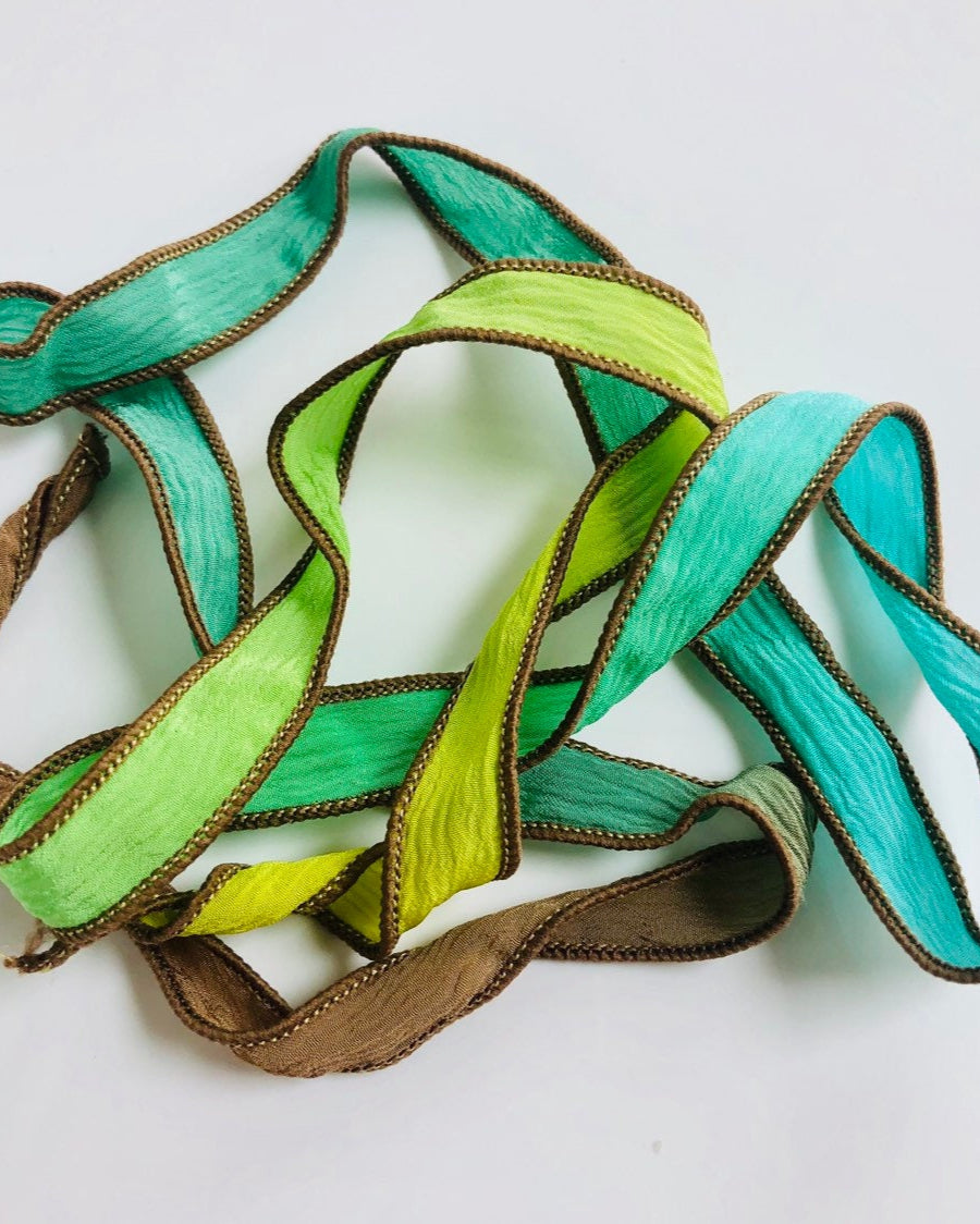 A silk wrap ribbon with hues of lime green, teal, forest green, and brown, with brown stitching, displayed on a white background.