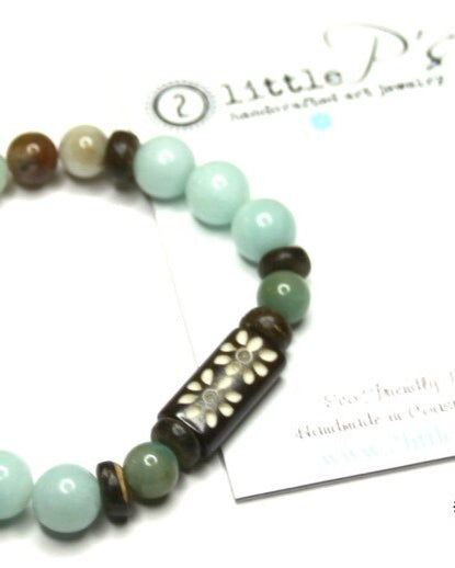 An elastic stretch bracelet with round and barrel-shaped beads in shades of brown and green, featuring a dragonfly focal bead and small wooden beads, displayed alongside its packaging with the brand '2 Little P's'.