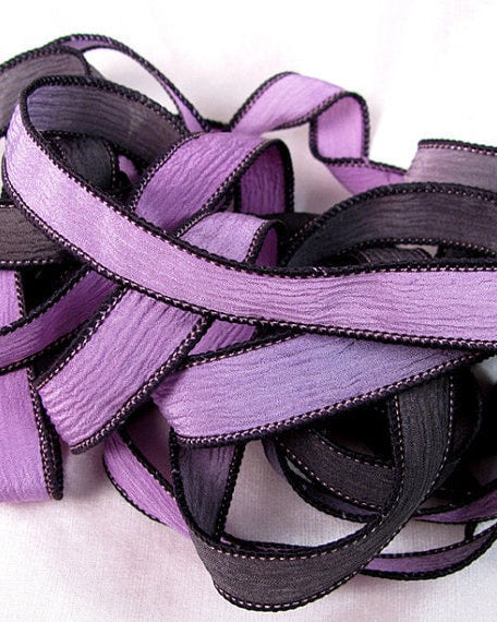 A coiled silk wrap ribbon in hues of lavender and jet black, displaying a crinkled texture.