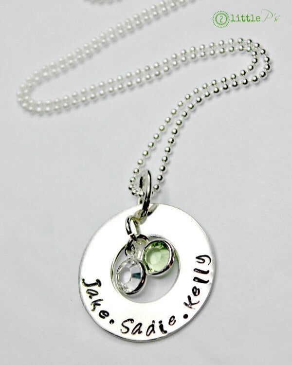 A sterling silver necklace with a hand-stamped washer charm featuring names and a birthstone charm with a Swarovski crystal.