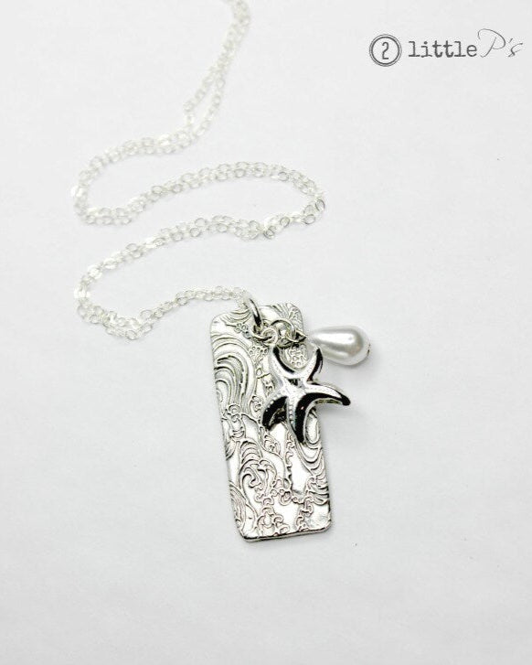 A silver pendant necklace featuring a handcrafted design with a pearl and sterling silver star fish, hanging on a white background.