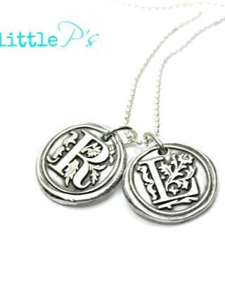 A sterling silver necklace with two circular wax seal charms attached to it, suspended from a silver ball chain.