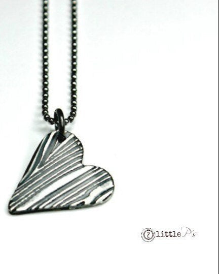 A silver heart-shaped pendant with a tree bark texture, suspended from an oxidized sterling silver ball chain.