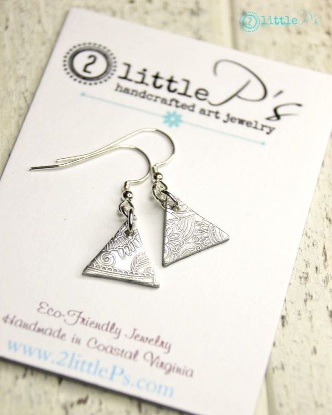 A pair of handcrafted silver earrings with a floral pattern, displayed on a card labeled '2 little P's - handcrafted art jewelry'.