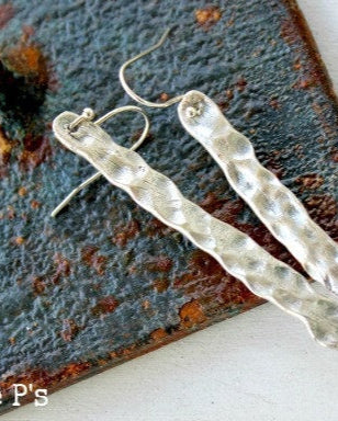A pair of silver hammered earrings laid on a textured surface.