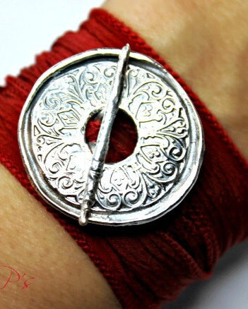 A person wearing a red silk wrist wrap bracelet with a silver mandala toggle clasp.