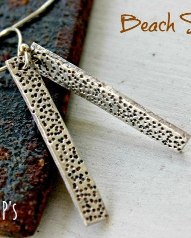 A pair of silver earrings designed to resemble grains of beach sand, with the brand '2 LITTLE P'S' visible.