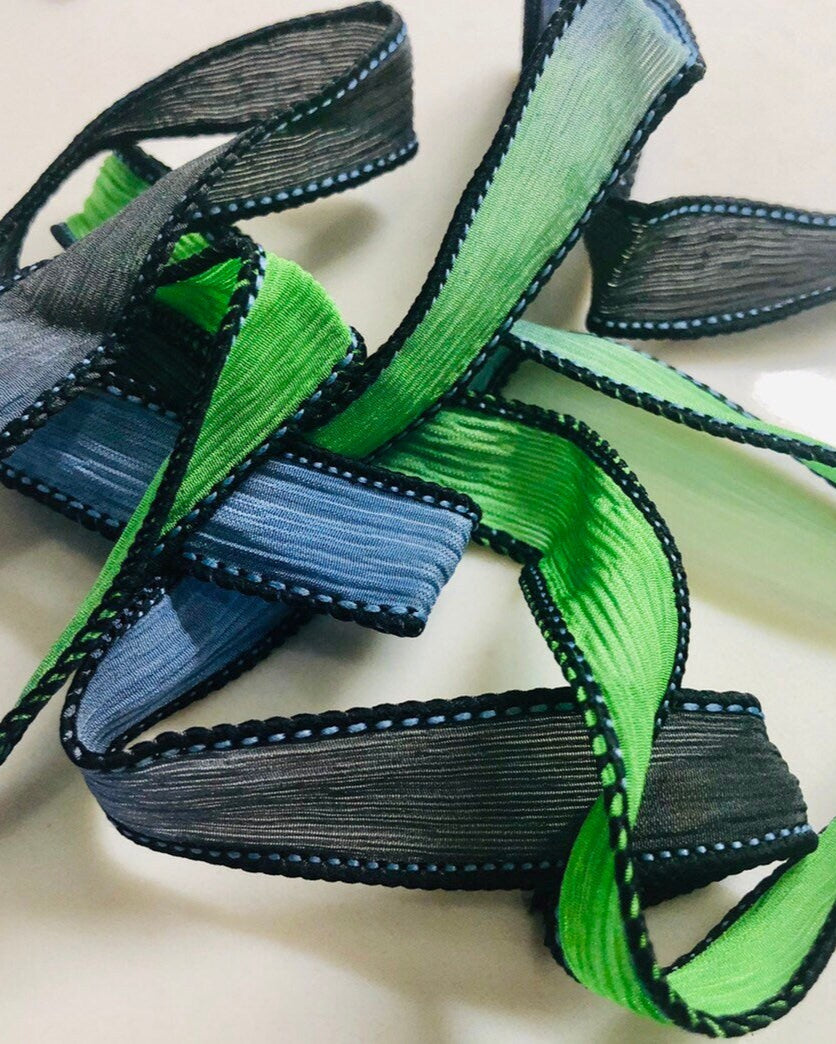 A silk wrap ribbon with hues of lime green, gray, and jet black, sewn to a point.