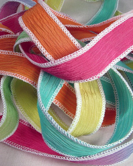 A collection of colorful silk wrap ribbons in hues of yellow, pink, orange, yellow, and mint, arranged in a tangly mess.
