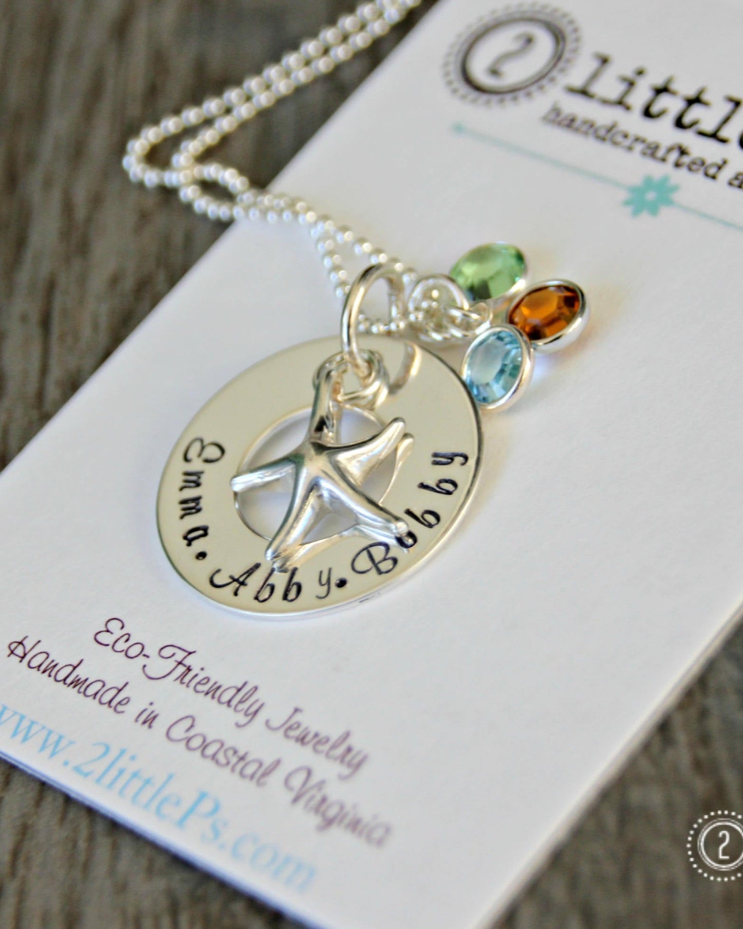 A sterling silver hand-stamped necklace with a starfish charm and Swarovski birthstone drops, displayed on a card with the brand name '2 Little P's'.