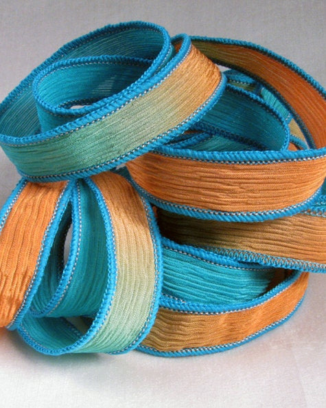 A stack of silk wrap ribbons with hues of coral and turquoise, each rolled up and secured with a blue tie.
